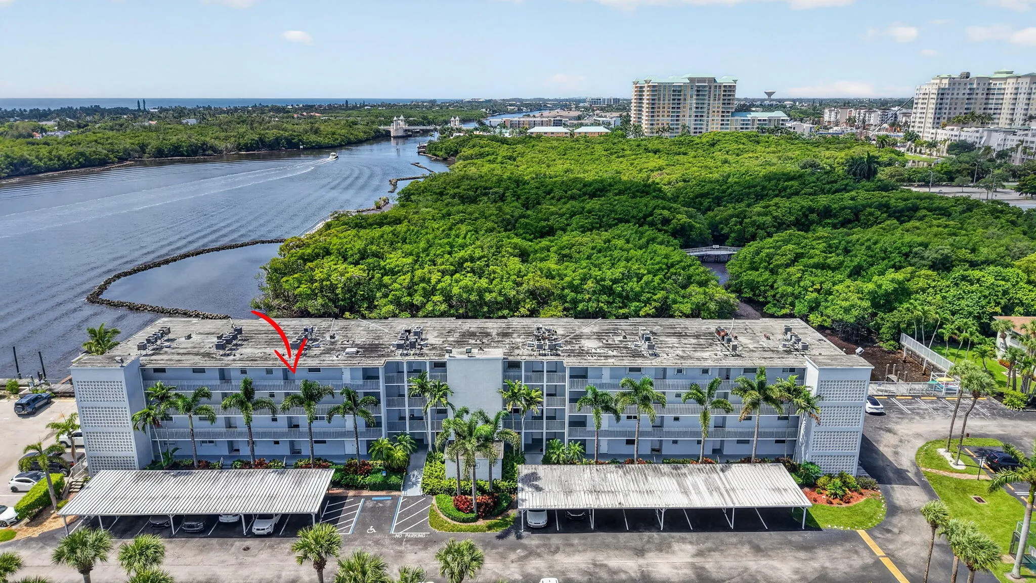 Multi-story building featuring covered parking, mature palm trees, waterfront access, and proximity to green space and urban amenities