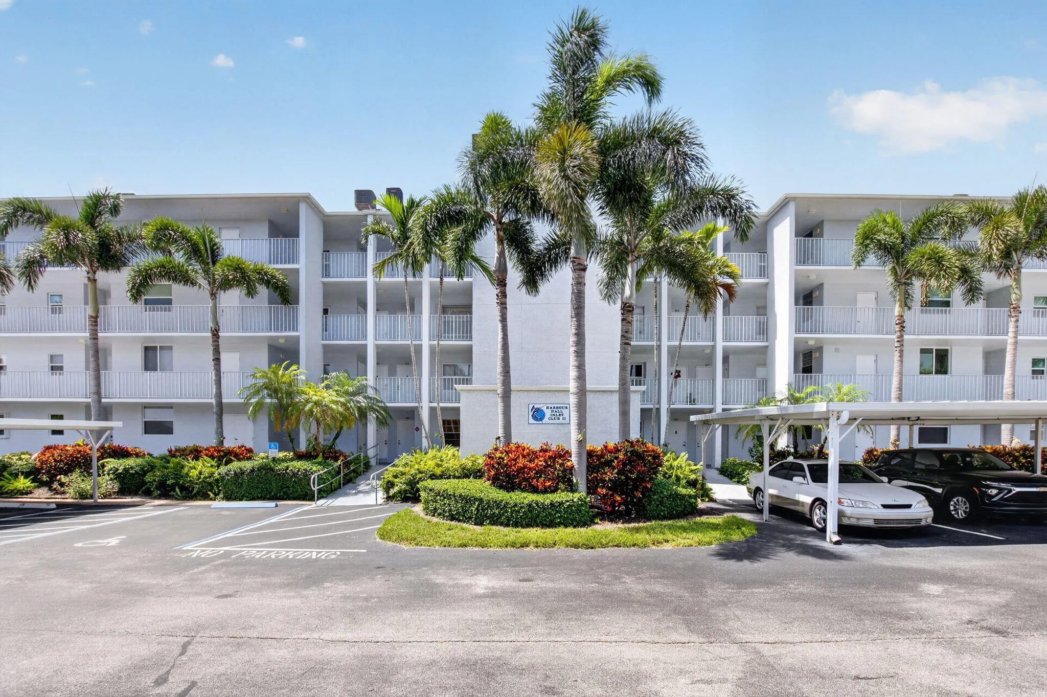 Multi-story condominium building featuring gray exterior, private balconies with white railings, and tropical landscaping