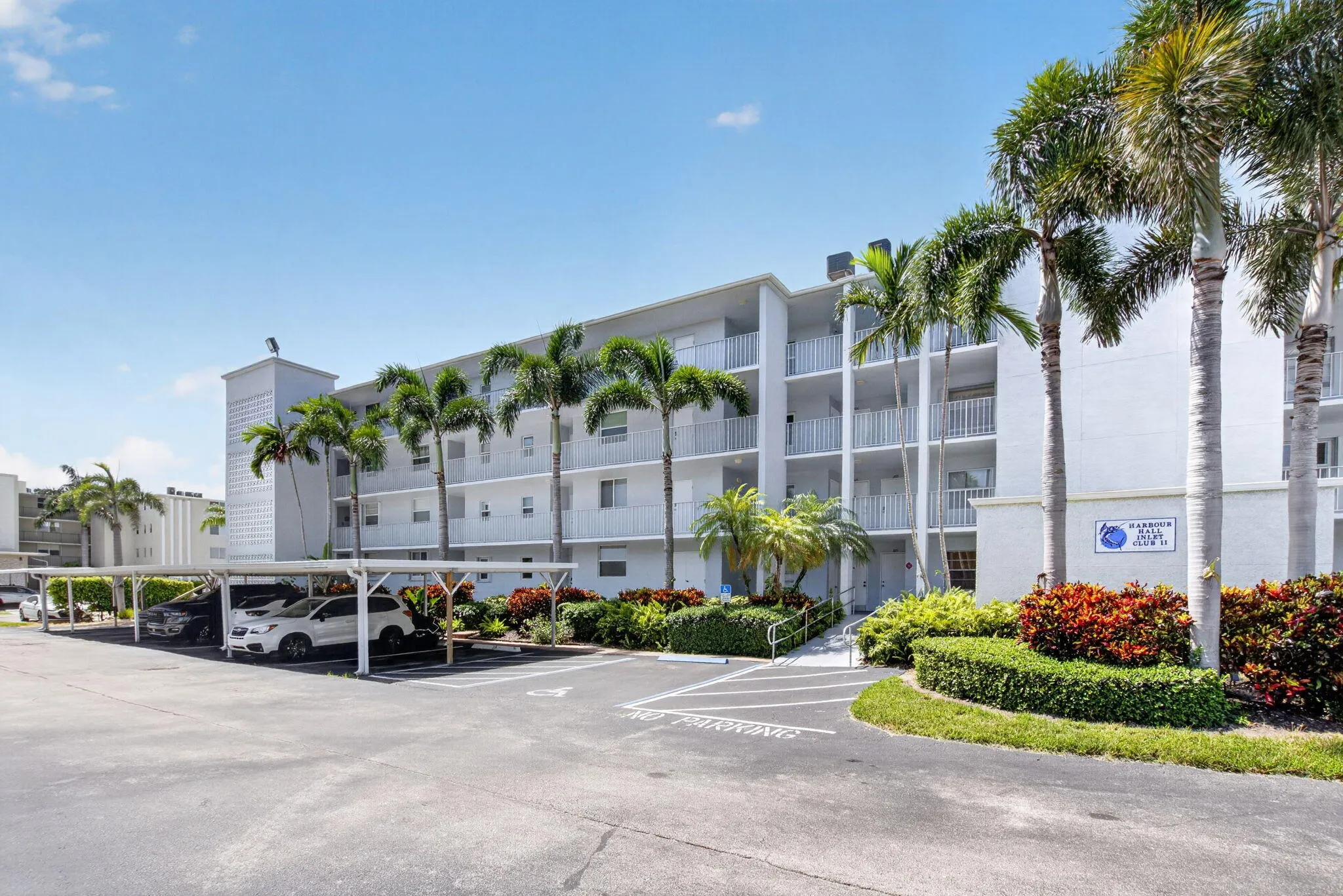 Multi-story building exterior with individual balconies, mature palm trees, and carports