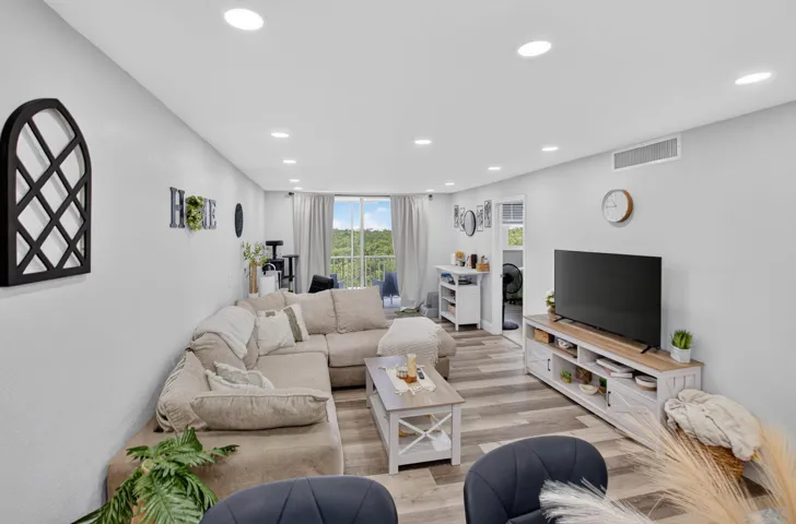 Spacious living area featuring light-colored walls, recessed ceiling lights, and wood-finish flooring