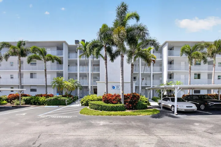 Multi-story condominium building featuring gray exterior, private balconies with white railings, and tropical landscaping