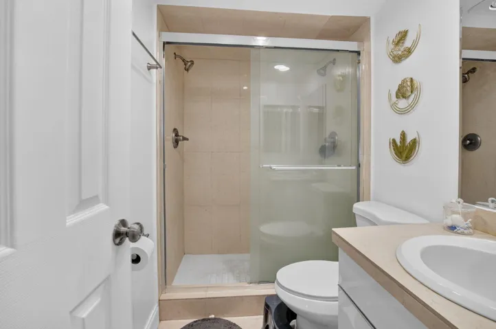 Bathroom featuring a glass-enclosed shower with tile surround, a single vanity with an integrated sink and light-toned countertop, and a white toilet