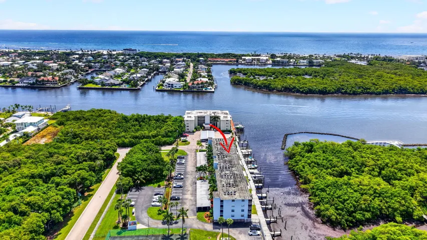 Aerial property perspective featuring a waterfront building with boat slips, surrounded by lush green foliage and open water access to the ocean