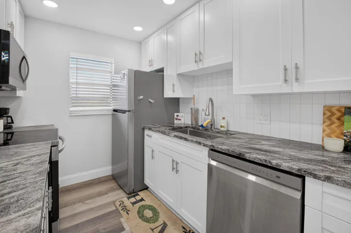 Modern kitchen featuring white shaker cabinetry with brushed nickel hardware, stainless steel appliances, dark stone countertops, and a white subway tile backsplash