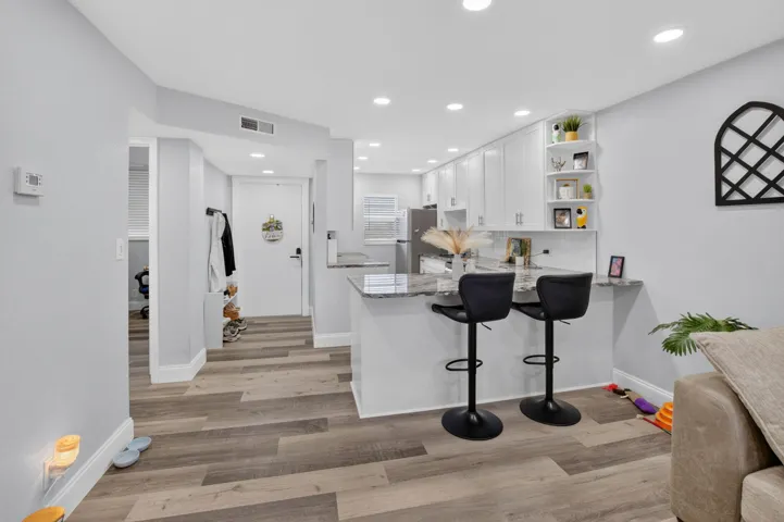 Modern kitchen featuring white shaker cabinetry, stainless steel appliances, a breakfast bar with stone countertops, and recessed lighting