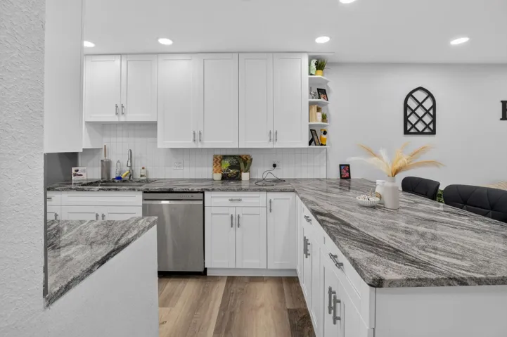 Modern kitchen featuring white shaker cabinetry, stainless steel dishwasher, recessed lighting, and a wrap-around countertop with a grey and white marbled pattern