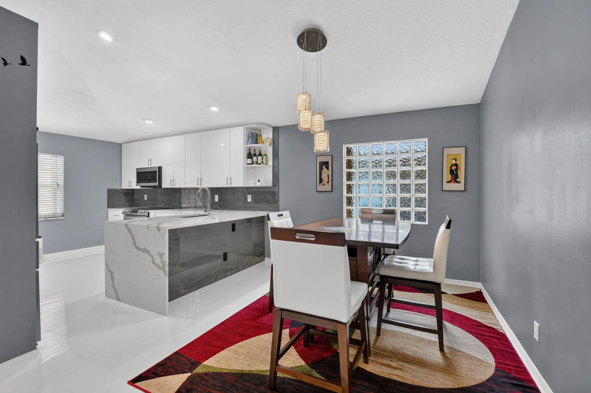 Open-concept kitchen and dining area featuring a waterfall island with stone countertop, white gloss cabinetry, recessed lighting, and a glass block window