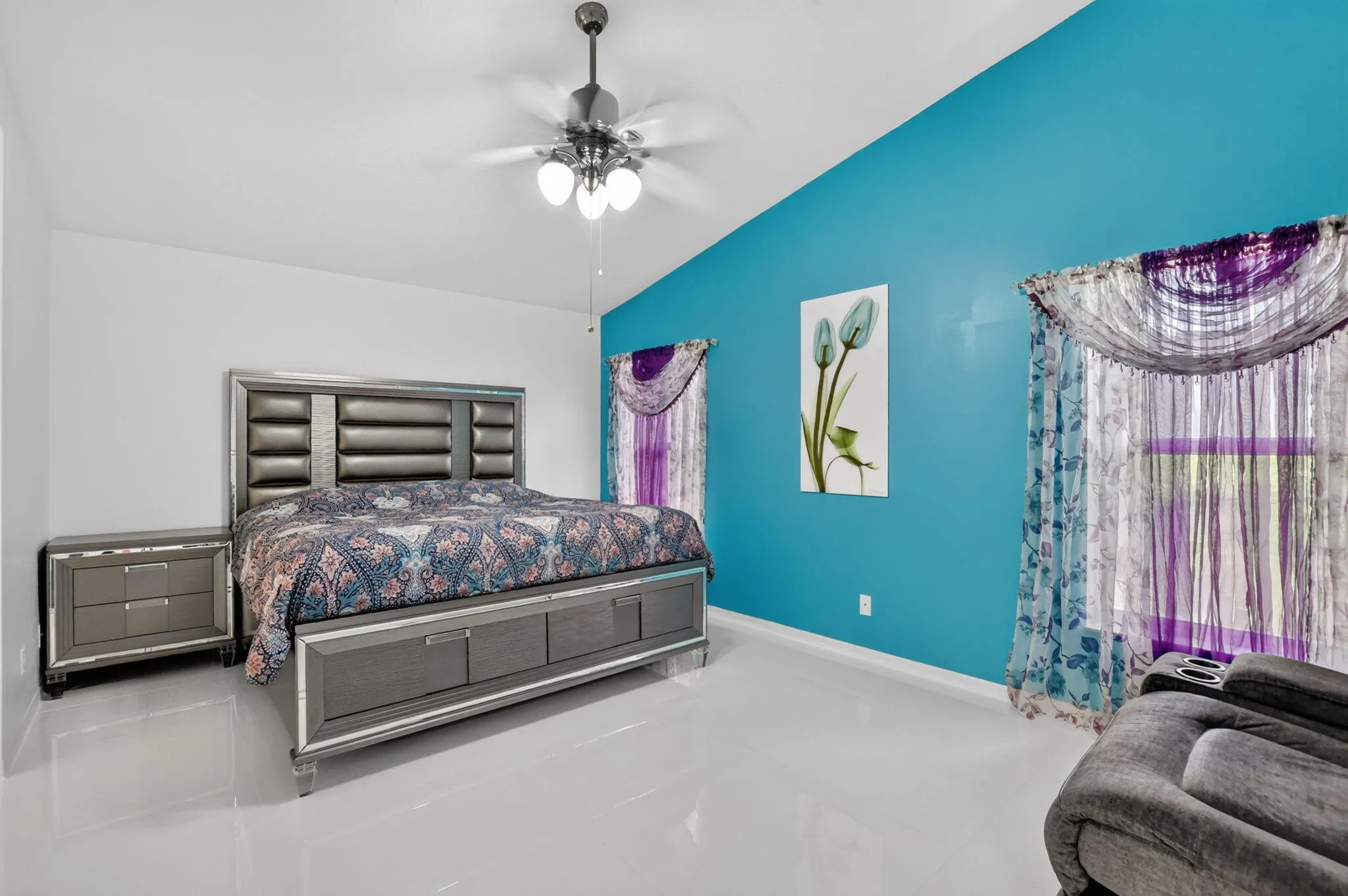 Bright room featuring a vaulted ceiling with a ceiling fan, white flooring, and a vibrant accent wall