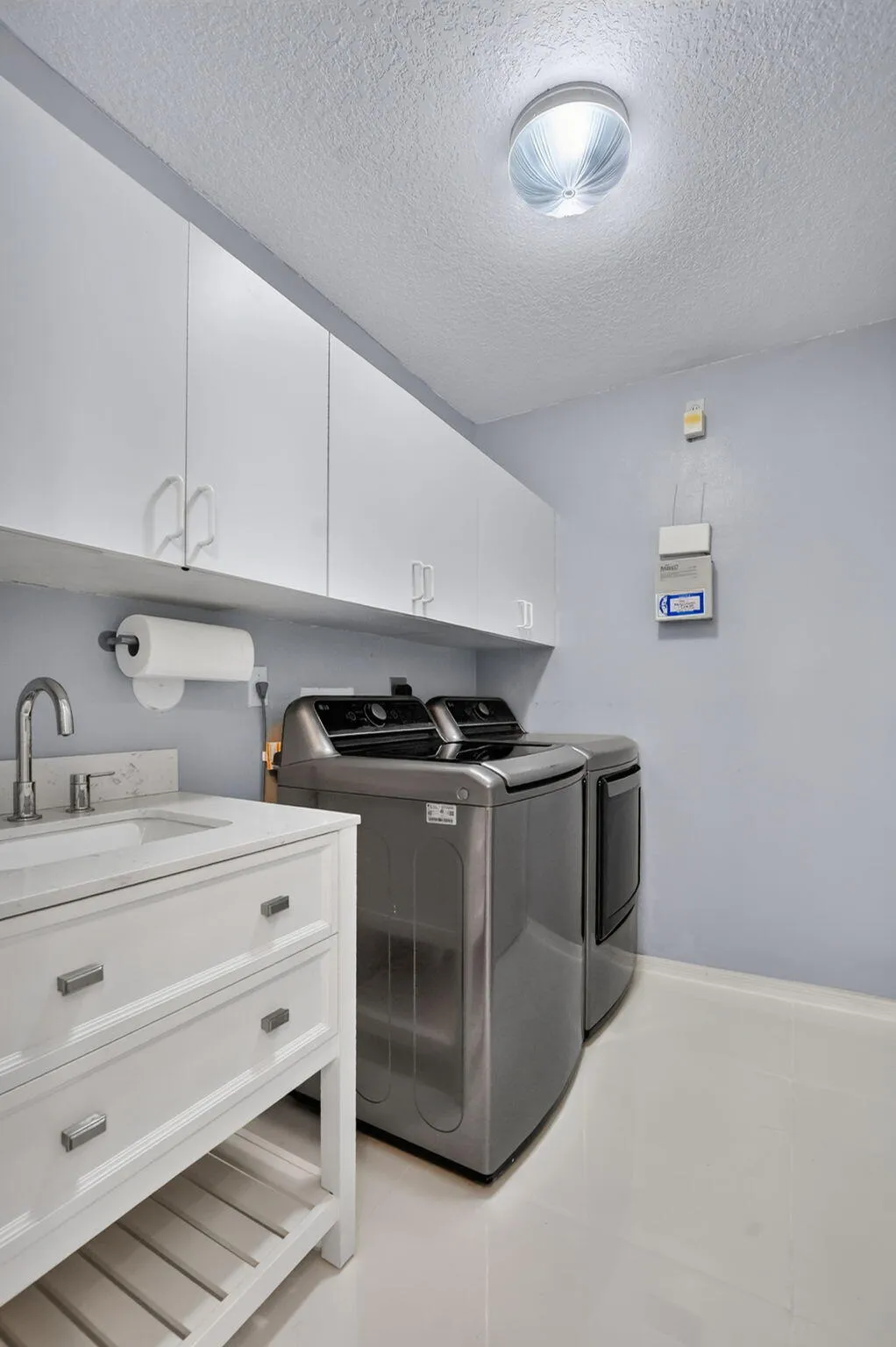 Dedicated laundry area featuring a white vanity with integrated sink, chrome faucet, white upper cabinetry, and light-toned flooring