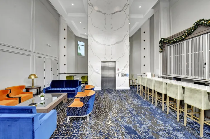 Lobby area featuring a high ceiling, wainscoting, a textured accent wall with integrated elevator, a built-in bar with seating, and patterned carpeting