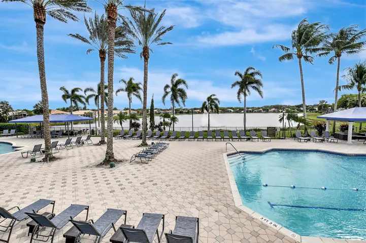 Community pool with a paver deck, surrounded by palm trees and overlooking a body of water