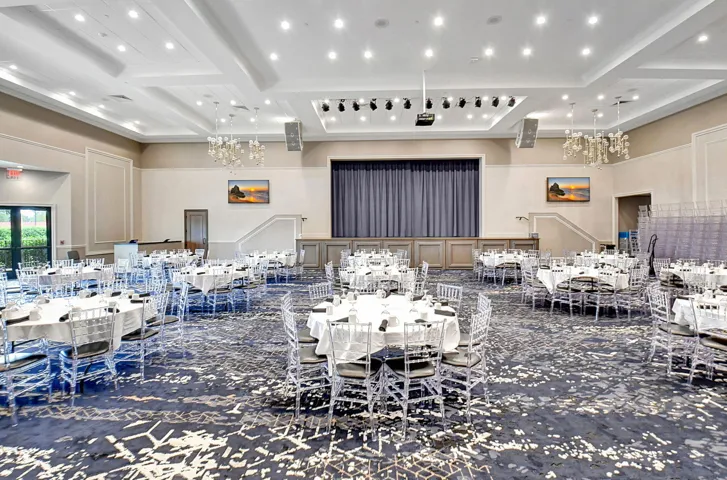 Spacious event hall featuring a recessed stage with dark drapery, a coffered ceiling with recessed lighting, and ornate wall paneling