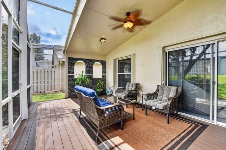 Screened outdoor living area featuring wood-finish flooring, a ceiling fan with light fixture, and a textured accent wall with integrated niches