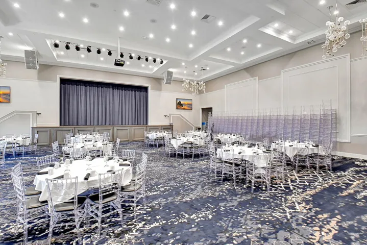 Spacious event hall featuring a stage with dark curtains, recessed lighting, and decorative wall paneling