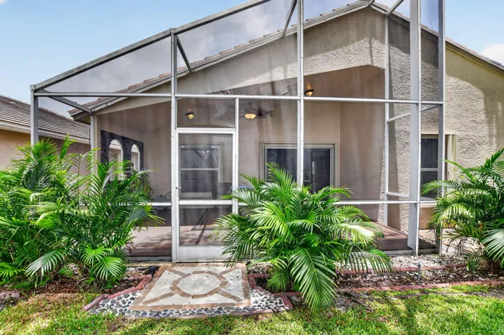 Screened patio area featuring a textured stucco exterior, tiled roofline, and established shrubbery