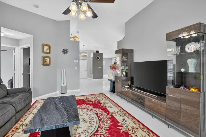 Vaulted ceiling living area featuring light gray walls, white tile flooring, and a ceiling fan with integrated lighting