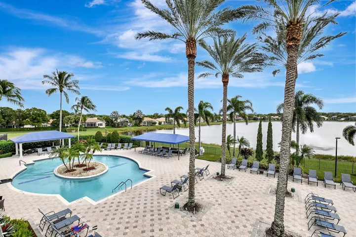 Resort-style pool with a central palm-lined island, surrounded by an expansive paver patio