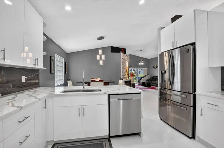 Modern kitchen featuring white cabinetry, quartz countertops, a stainless steel refrigerator, and a built-in dishwasher
