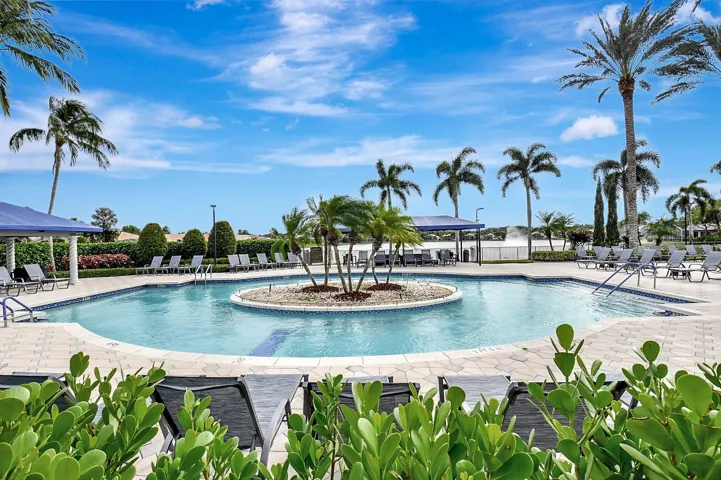 Resort-style swimming pool featuring a central island with palm trees, a surrounding paved deck, and multiple lounge chairs