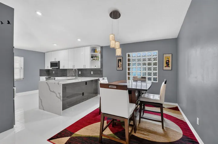 Open-concept kitchen and dining area featuring a waterfall island with stone countertop, white gloss cabinetry, recessed lighting, and a glass block window