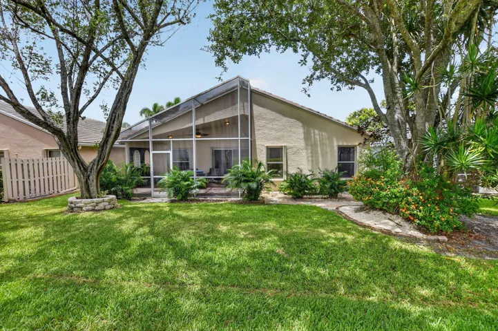 Expansive backyard featuring a screened patio enclosure, a manicured lawn, established trees, and mature landscaping
