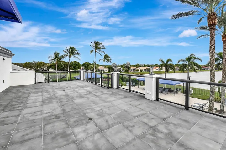 Spacious outdoor terrace with large format grey tile flooring, glass panel railing, and water frontage