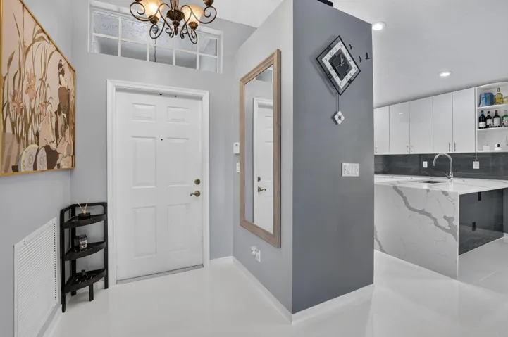 Entryway featuring a white paneled door with transom window, overhead chandelier, and a mirror with a wood-finish frame