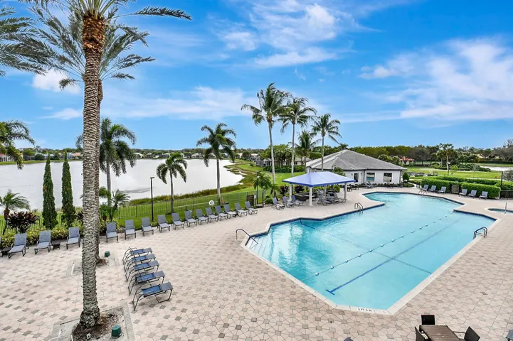 Resort-style aquatic amenity featuring a large swimming pool with lap lanes, expansive paver decking, and a shaded outdoor seating area