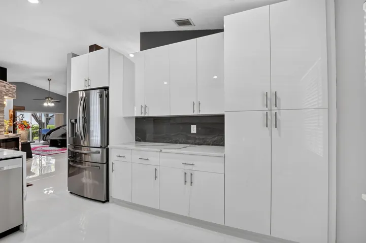 Contemporary kitchen featuring white high-gloss cabinetry, stainless steel refrigerator, white countertops, dark backsplash, and polished flooring