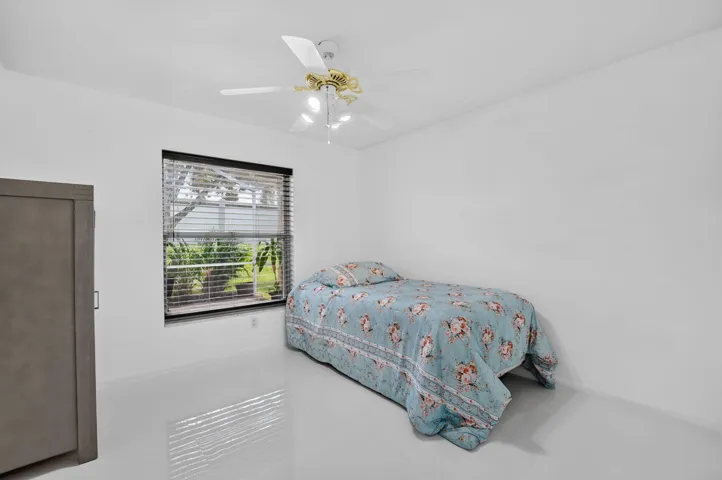 Bright interior space featuring a window with horizontal blinds, a ceiling fan with integrated lighting, and light-toned flooring