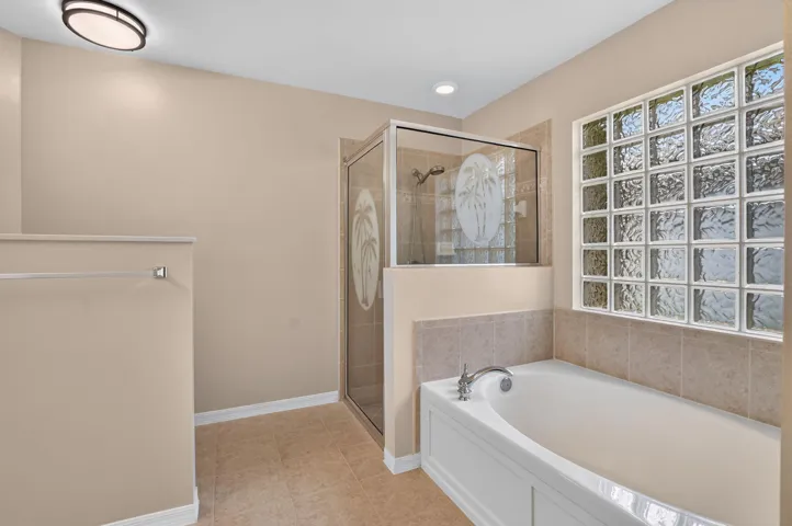 Bathroom featuring a glass block window, a built-in tub with a deck-mounted faucet, and a tiled shower with a clear glass enclosure and etched detailing