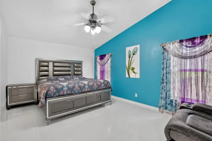 Bright room featuring a vaulted ceiling with a ceiling fan, white flooring, and a vibrant accent wall