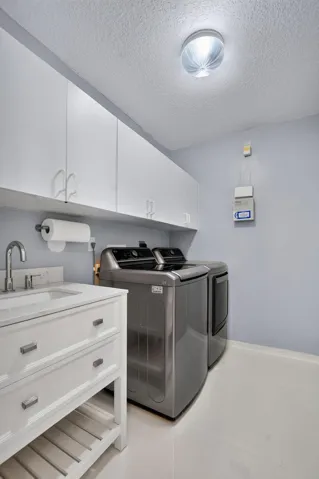 Dedicated laundry area featuring a white vanity with integrated sink, chrome faucet, white upper cabinetry, and light-toned flooring