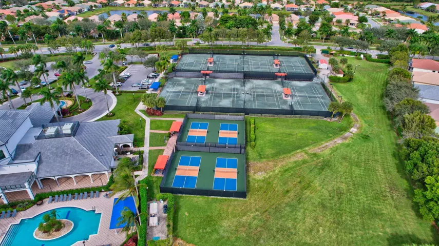 Community amenities featuring multiple tennis courts, pickleball courts, a clubhouse with a grey roof, an adjacent swimming pool, and landscaped grounds