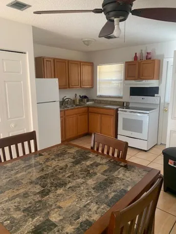 Kitchen featuring wood cabinetry, white appliances, and light-toned tile flooring