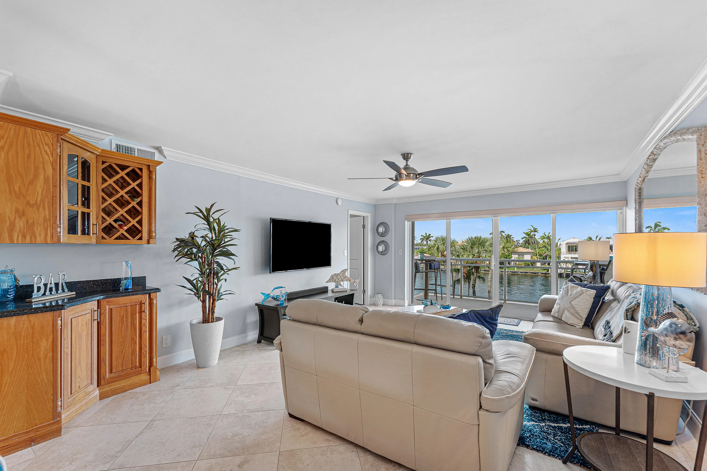 Living area with large format tile flooring, crown molding, and a built-in wet bar featuring wood cabinetry, a wine rack, and a dark stone countertop