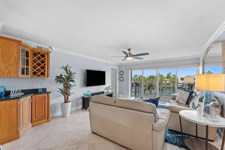 Living area with large format tile flooring, crown molding, and a built-in wet bar featuring wood cabinetry, a wine rack, and a dark stone countertop