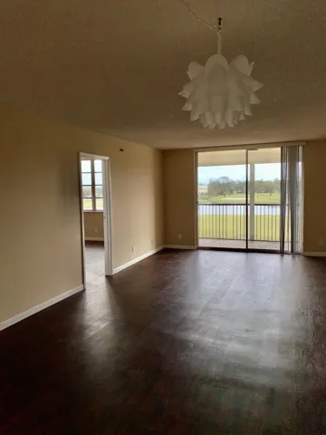 Spacious room featuring dark wood-finish flooring, neutral wall tones, and a distinctive chandelier