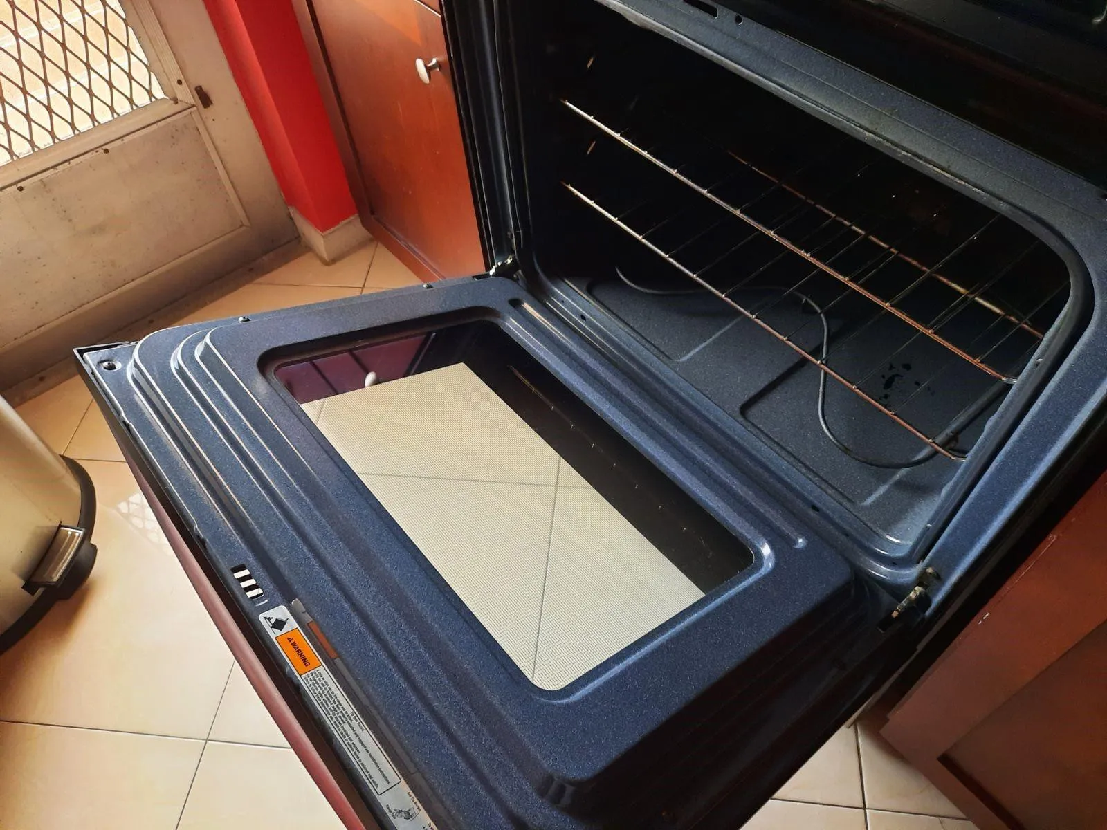 Integrated oven with a dark interior, featuring multiple wire racks, a glass oven door, and a tiled floor surround