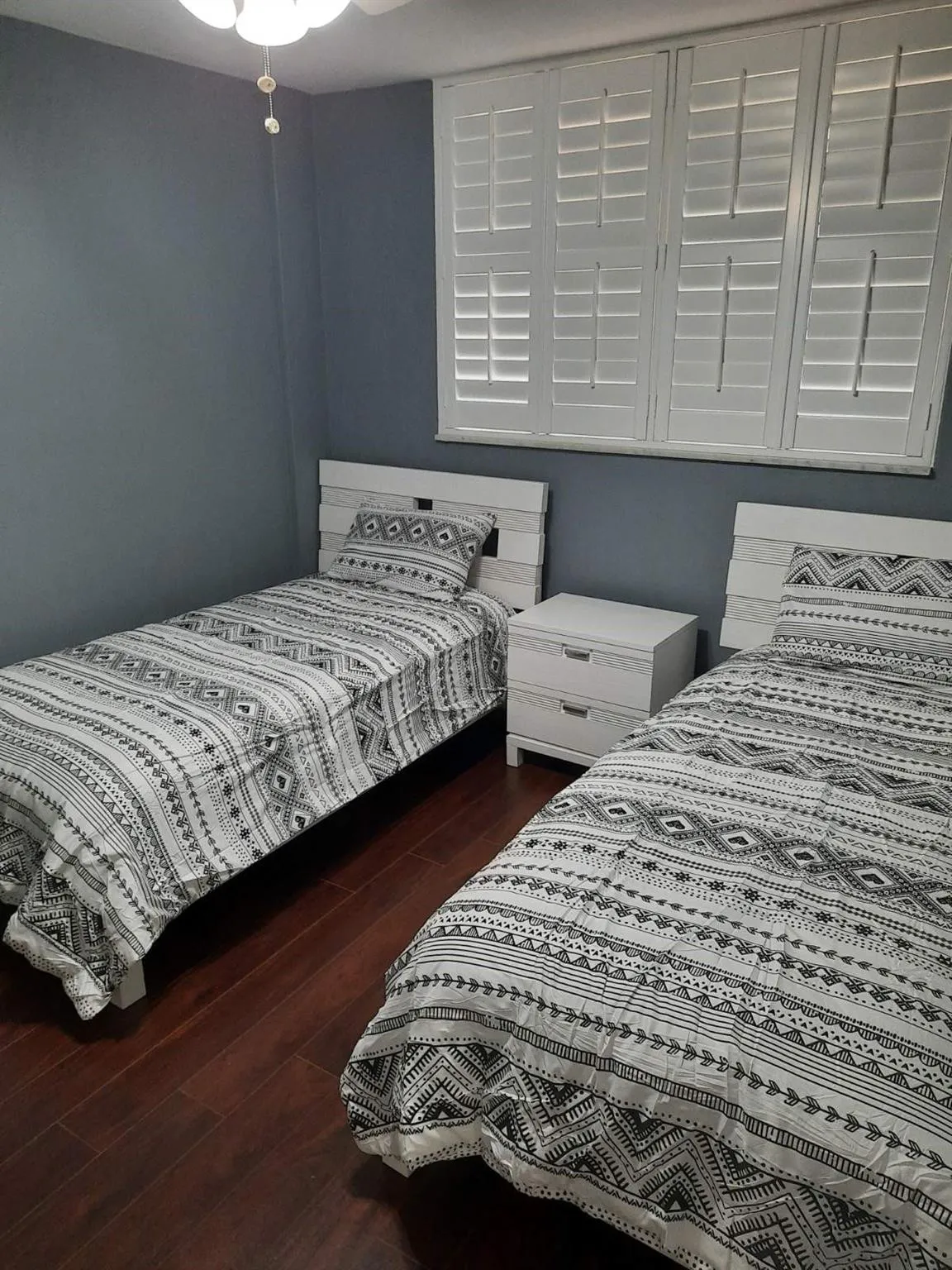 Bedroom featuring dark wood-finish flooring and a window with white plantation shutters