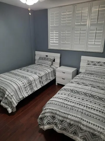 Bedroom featuring dark wood-finish flooring and a window with white plantation shutters