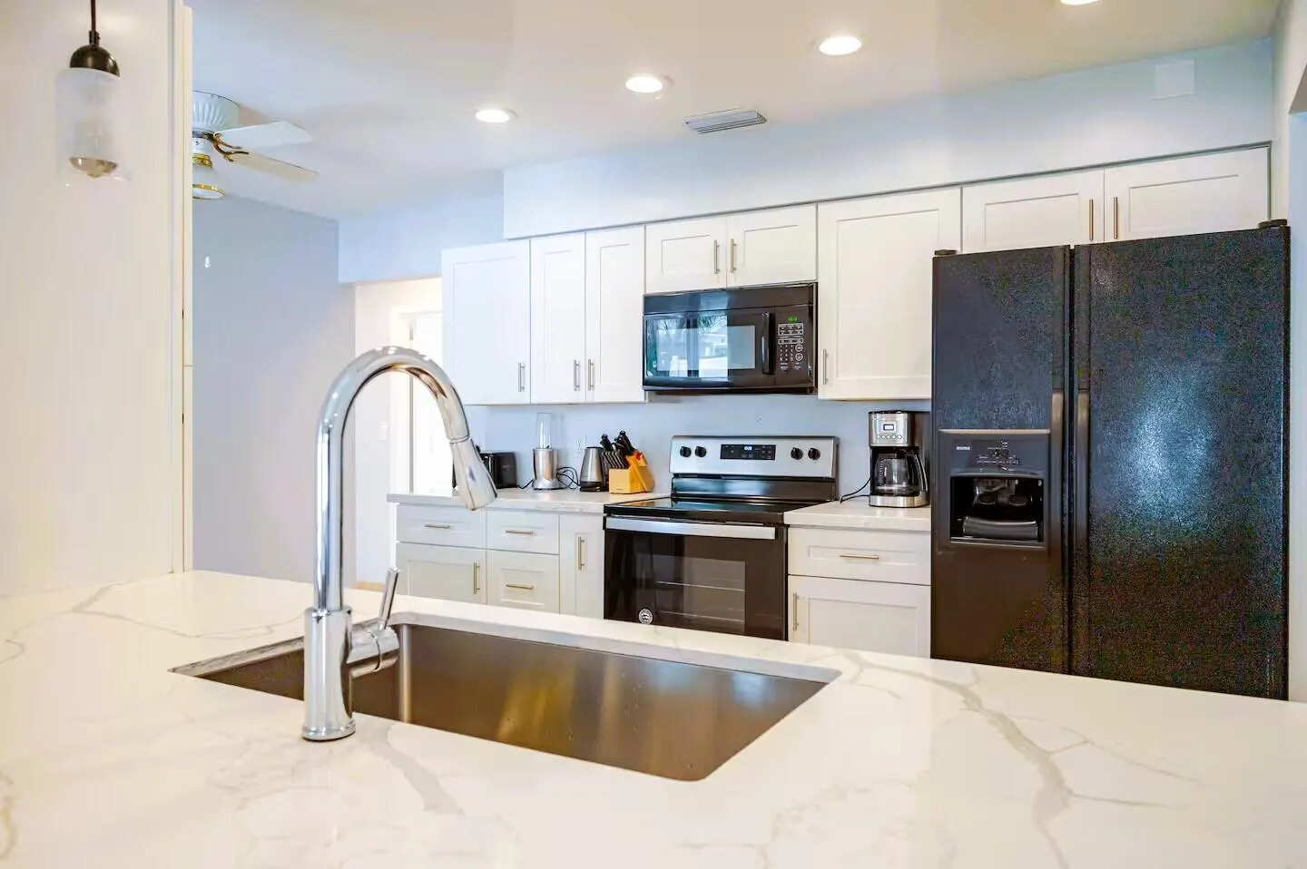 Kitchen featuring white shaker cabinetry, stainless steel sink with gooseneck faucet, light-toned countertop with veining, black appliances, and recessed lighting