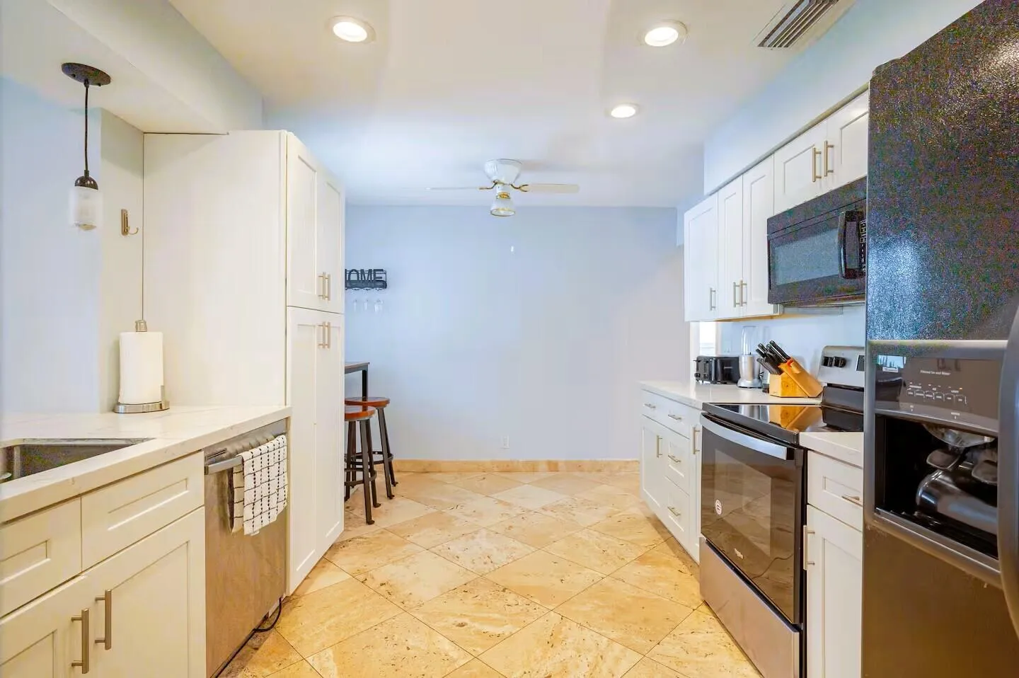 Galley kitchen featuring light-toned tile flooring, white cabinetry with gold-toned hardware, white countertops, and stainless steel appliances
