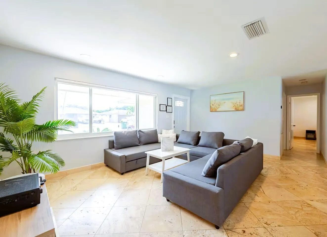Bright living space featuring large sliding windows, light-colored tile flooring, recessed ceiling lighting, and a white entry door with frosted glass