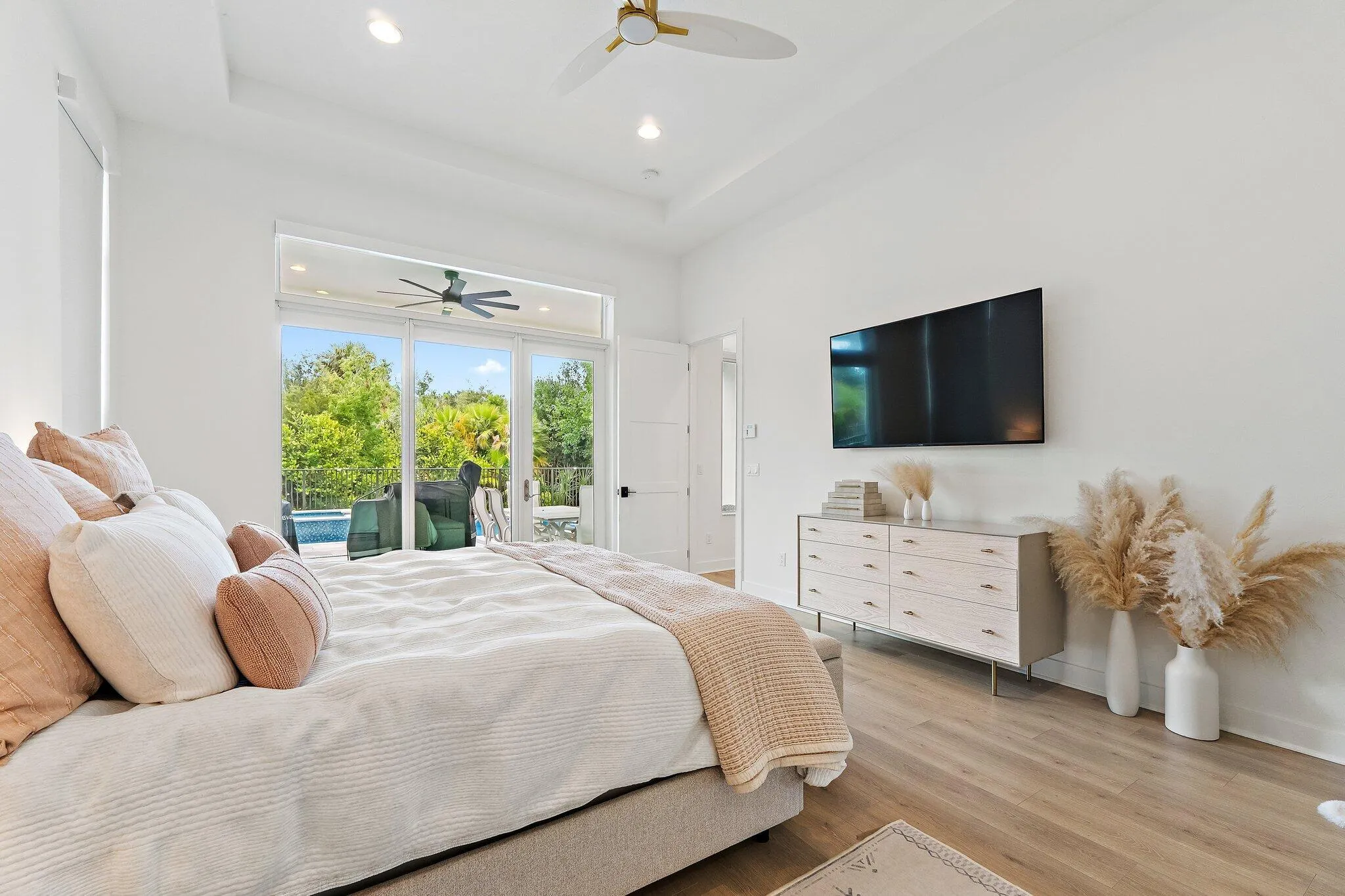 Bedroom with bed, nightstands, wall-mounted TV, ceiling fan, and sliding glass doors