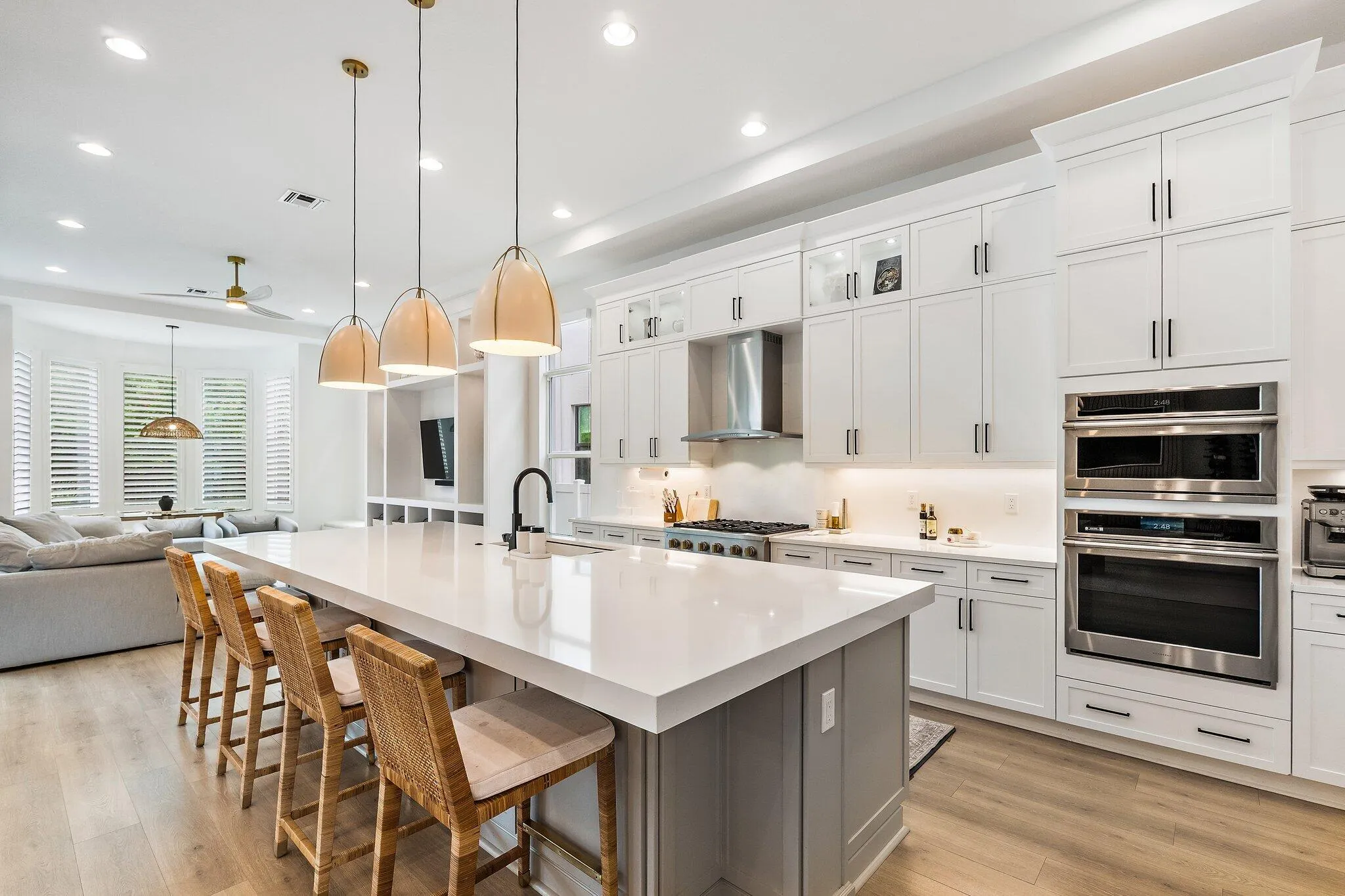 Kitchen with white cabinetry, large island, wood bar stools, and double wall ovens
