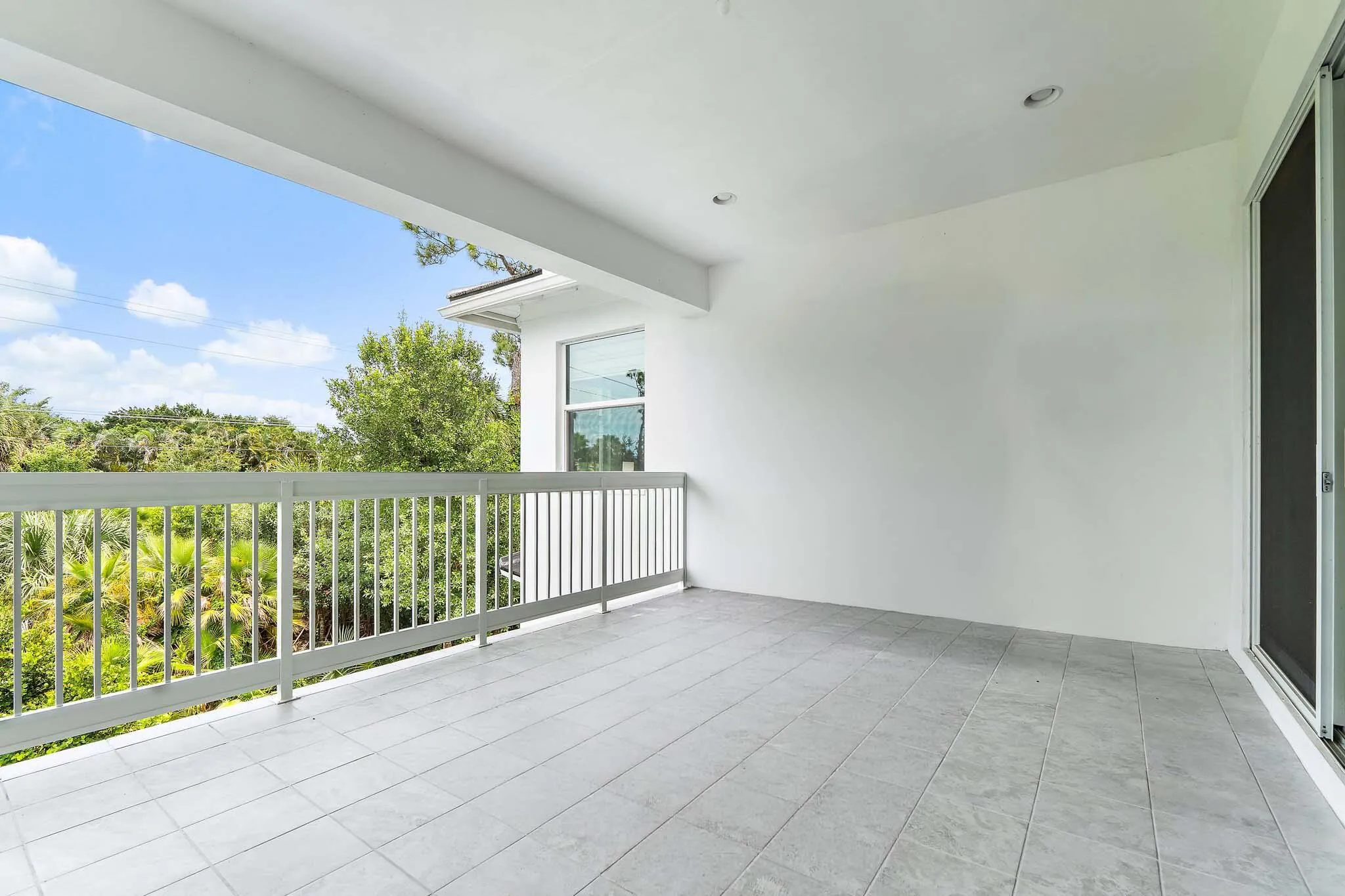 Covered balcony with railing, tile flooring, and lush green view