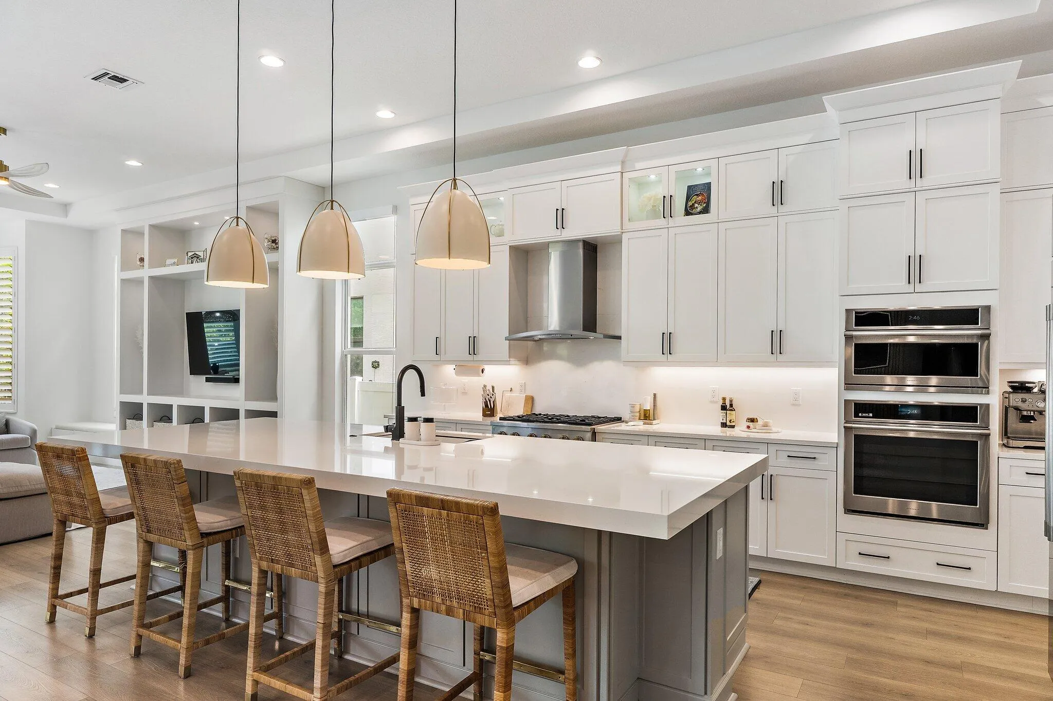 Kitchen with white cabinetry, large island, woven bar stools, and double wall ovens