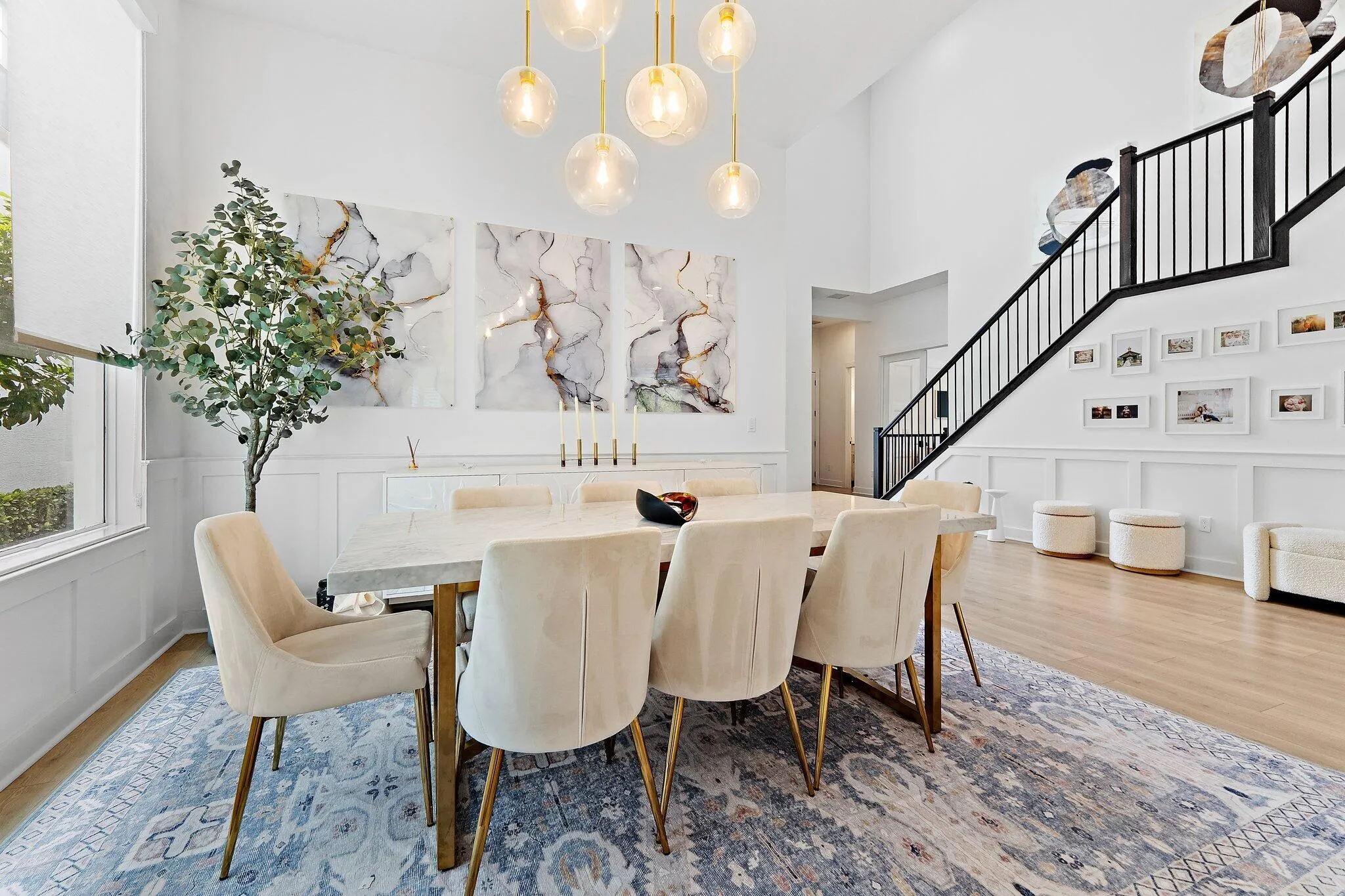 Dining area with round table, upholstered chairs, chandelier, and area rug near staircase