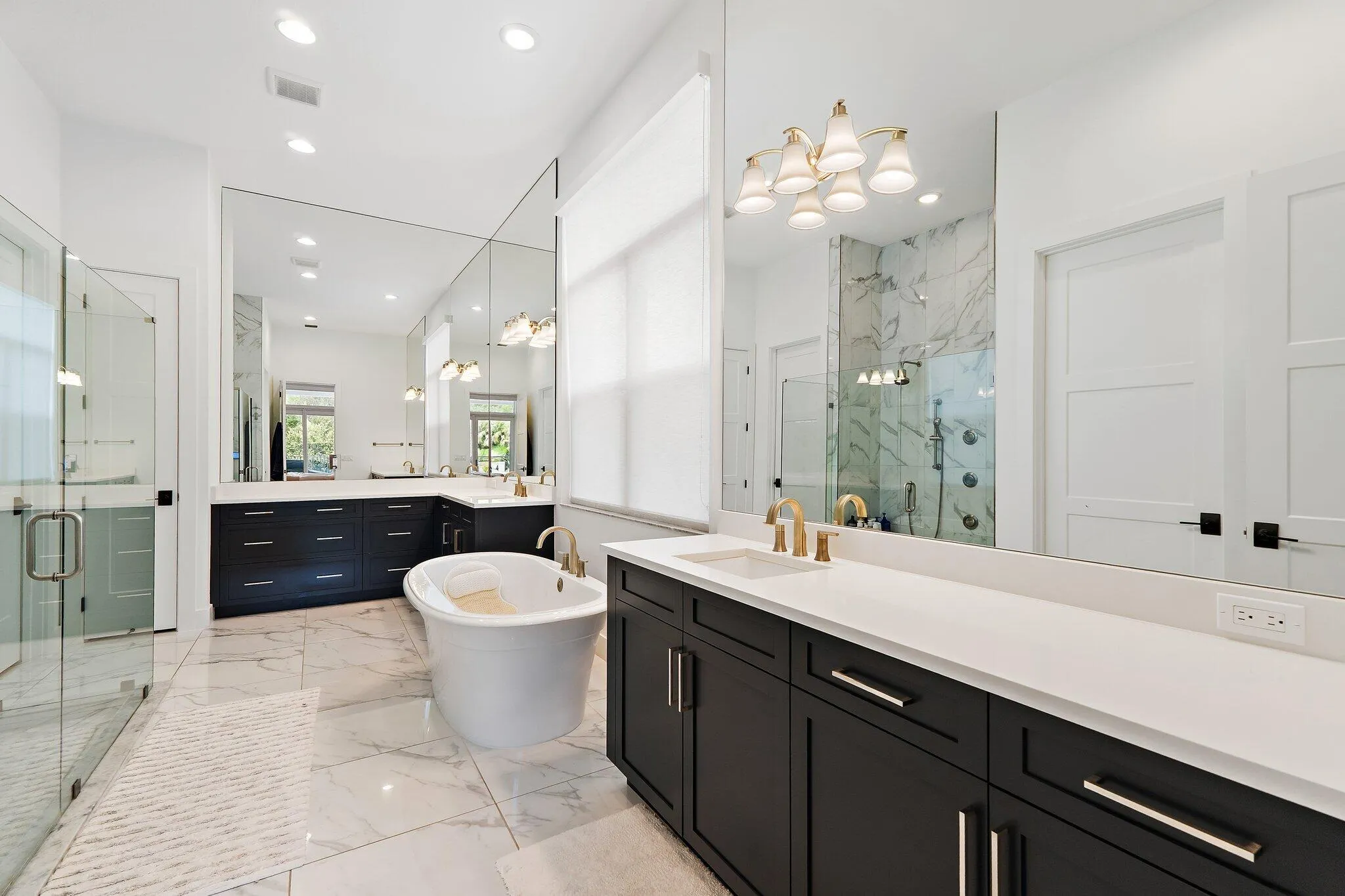 Primary bathroom with dual vanity, dark cabinetry, freestanding soaking tub, and glass shower